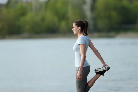 Side view portrait of a sportswoman stretching leg after sport in a lake