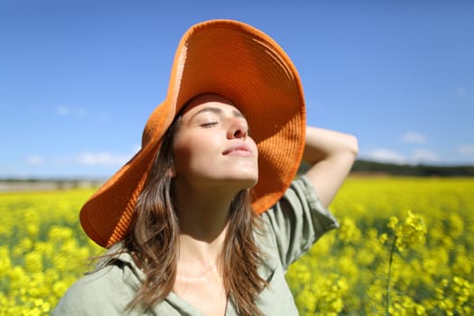 Satisfied woman with orange pamela breathing fresh air in a yellow flowered field