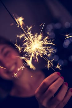 Smiling girl is holding a sparkler in her hand, indoor, lights in background