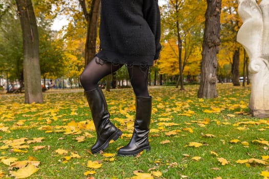 A girl in warm boots poses against a background of fallen foliage.