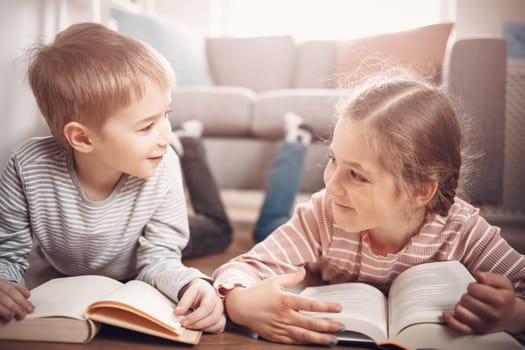 Cute children lying down on the floor and reading books. Concept of family and sibling relationships.