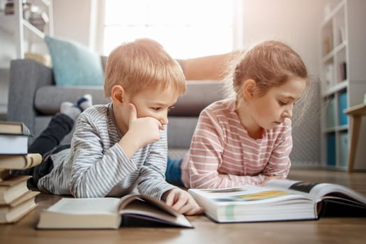 Cute children lying down on the floor and reading books. Concept of family and sibling relationships.