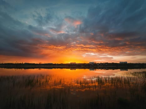 Colorful and dramatic sunset sky reflecting on pond water. Silent evening scene at Delia lake. Vibrant sundown clouds at the horizon over Ungheni city, Moldova. Reed and rush vegetation in the water