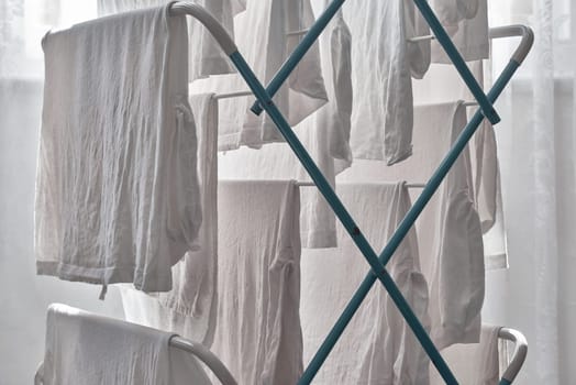 White washing hangs and dries on the racks of a clothes horse in the light of a bay window.
