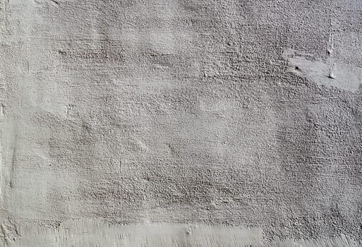 The heavy surface texture of an external wall covered in white plaster.