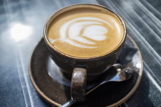 Cup of fresh made coffee with flower design in foam. Dark wooden table as background