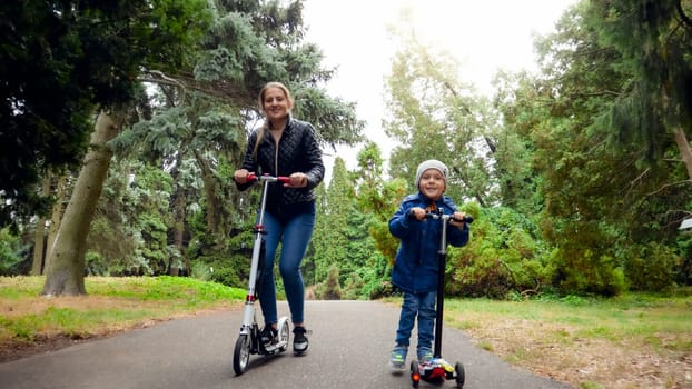 Happy smiling family riding on scooters at autumn park.