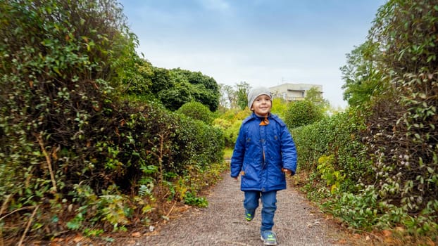 Happy smiling little boy running on narrow path at park or garden.