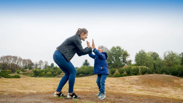 Happy smiling mother and little son standing on field and giving five each other.