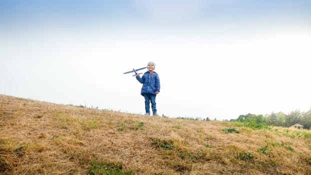 Happy smiling little boy standing on hill top with toy airplane.