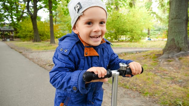 Portrait of smiling little boy smiling while riding on scooter at autumn park.