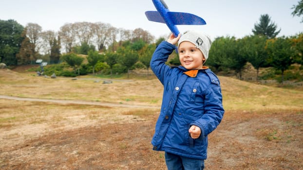 Portrait of smiling little boy throwing blue toy airplane in the field.