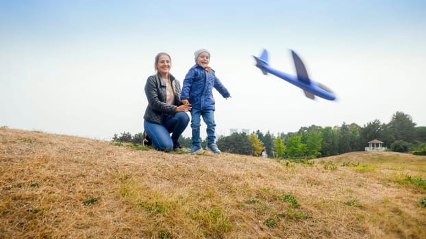 Happy excited little boy with mother throwing toy airplane from the hill at park.