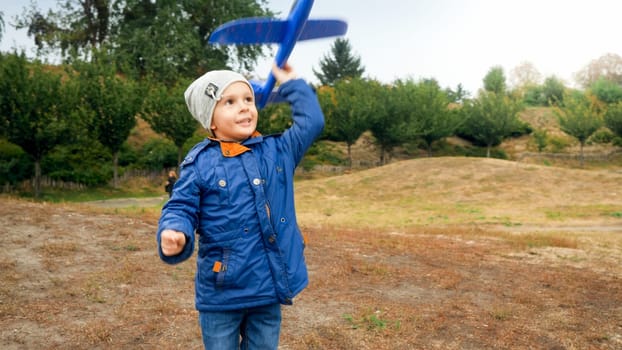 Happy smiling little boy launching and throwing toy airplane at autumn field.