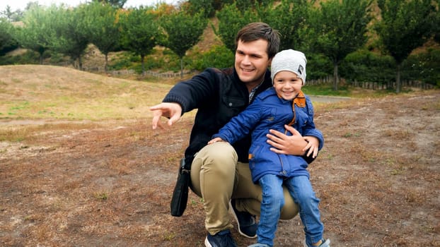 Happy young father hugging his little son and pointing with his finger at park.