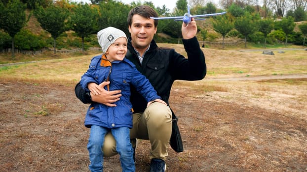 Portrait of happy laughing little boy with his father throwing toy airplane at park.