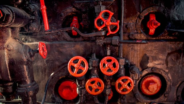 Toned image of old rusty steam pipes and red valves on steam boiler of old locomotive