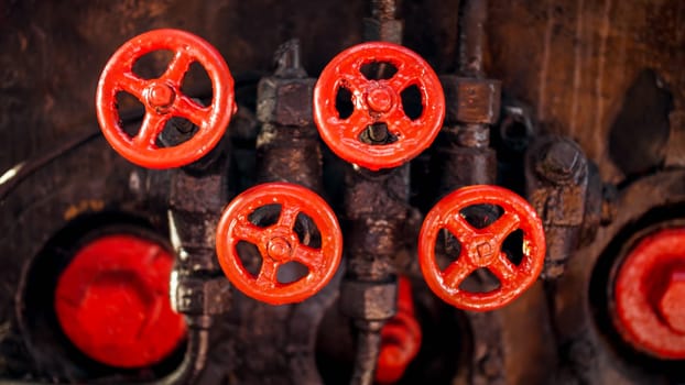 Closeup image of red painted vavles and black pipes of vintage high pressure system on factory