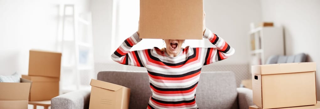 Tired woman with cardboard box on her head sitting on the sofa in her new house.Concept of renting, moving in new house and buying an real estate.