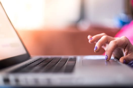 Girl with purple fingernails is using her laptop at home on the couch