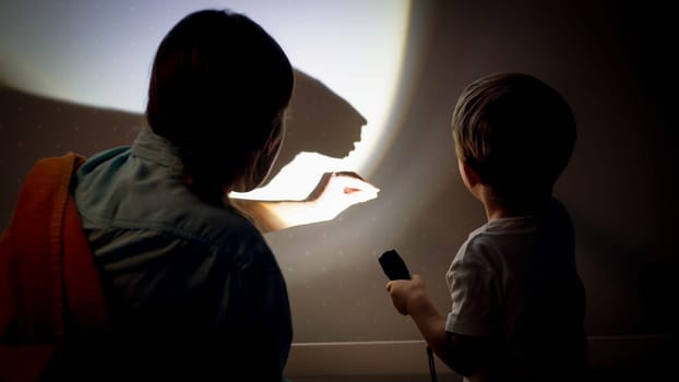 Closeup image of young mother teaching her little son showing shadows from torch on wall at night.