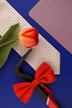 Still life with fashion accessories including an elegant necktie and red bowtie, spring tulip and blank sheet of notepaper with copyspace over a blue background