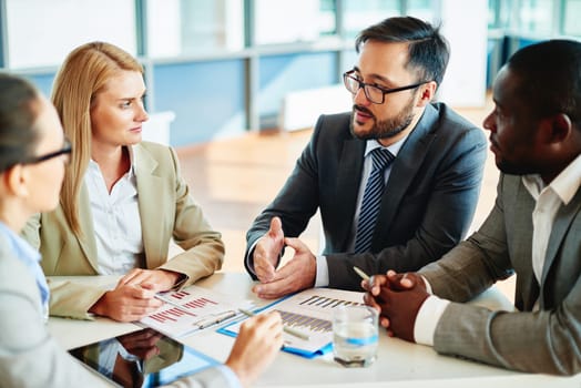 Serious businessman explaining principles of work to his colleagues at meeting