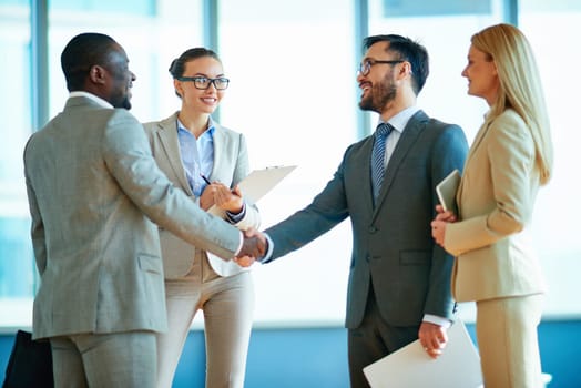 Happy businessmen handshaking with their two colleagues near by