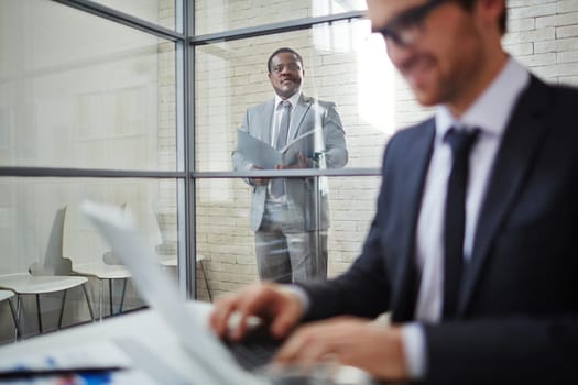 African businessman in suit looking at colleague working in office
