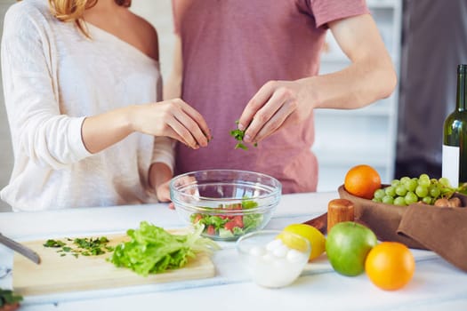 Hands of young couple adding cut parsley into bowl with fresh vegetarian salad