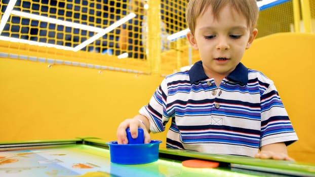 Cute excited boy palying air hockey in amusement park at shopping mall.