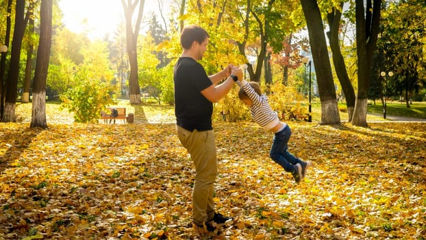 Young man playing and havng fun with his little son in autumn park.
