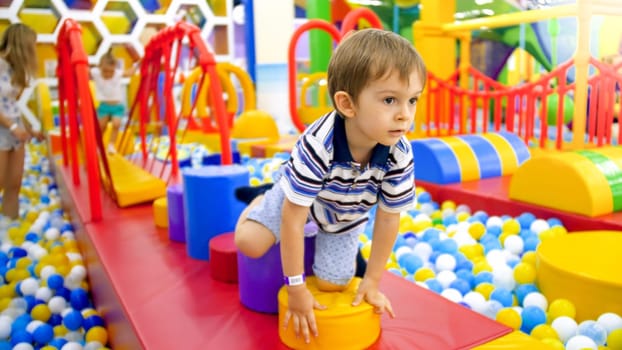 Cute little boy crawling and playing on colorful playground at shopping mall.