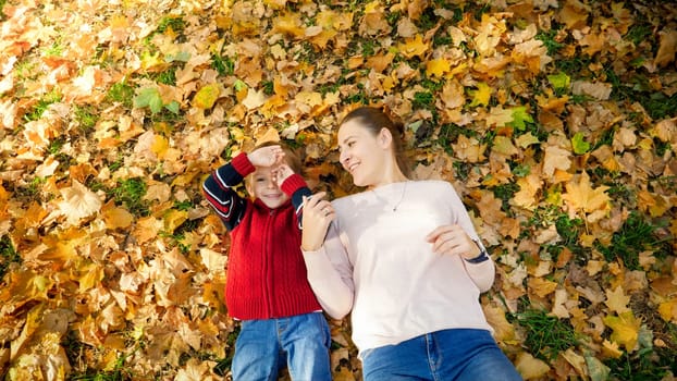 Portrait of happy smiling little boy lying on autumn leaves with his mother.