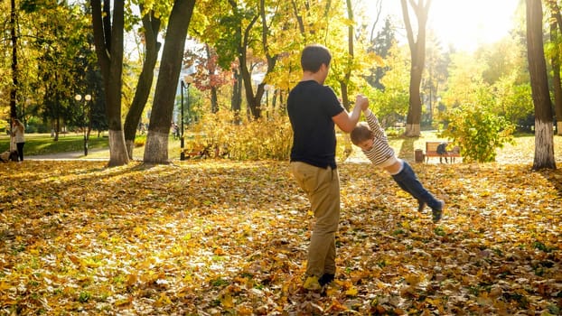 Young father holding his son by hands and spinning in autumn park.