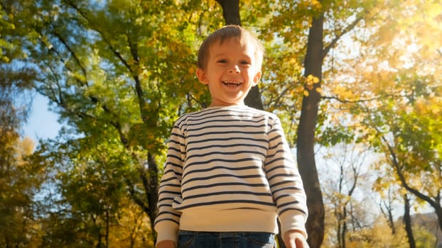 Portrait of happy smiling boy looking down at camera in autumn park.
