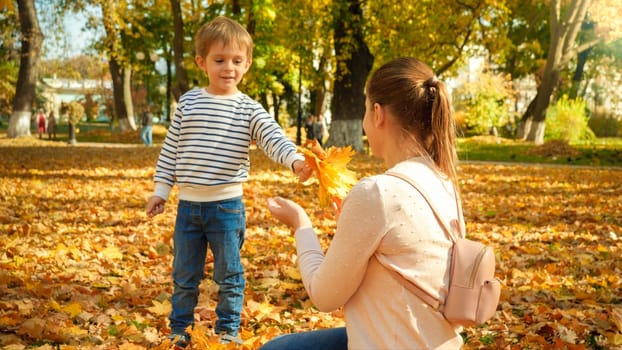 Happy smiling little boy with mother in autumn park covere with fallen yellow leaves.