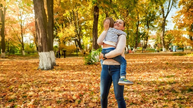 Beautiful smiling young mother hugging her little son in autumn park.