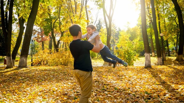 Young father holding and spinning his little son in autumn park.