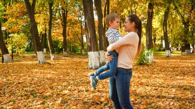 Portrait of happy smiling young mother embracing her little son in autumn park.