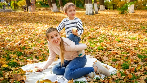 Funny image of little boy riding on mother's back in autumn park.