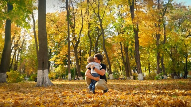 Adorable little boy hugging and kissing his father in autumn park.
