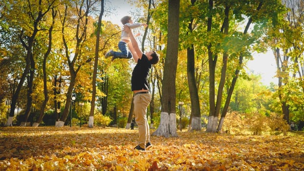 Happy young father playing and lifting up his little son in autumn park.