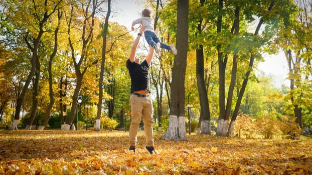 Young handsome man throwing up his little son at atumn park.