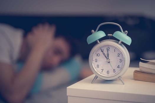 White alarm clock on the bedside table. Young man sleeps in the background.