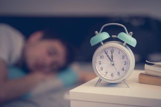 White alarm clock on the bedside table. Young man sleeps in the background.