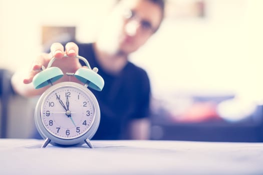 Man is pushing an alarm clock, sunshine in the morning, blurry background