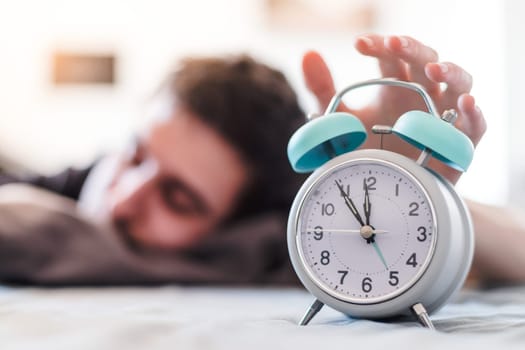 White alarm clock in the morning. Young man wakes up.
