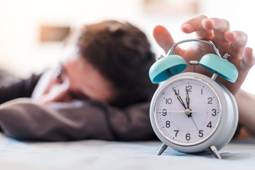 White alarm clock in the morning. Young man wakes up.