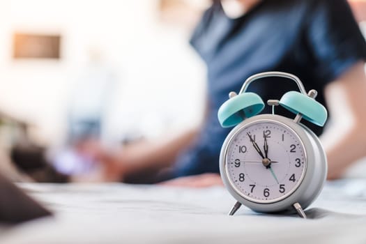 White alarm clock in the morning. Young man wakes up and stretches in the background.